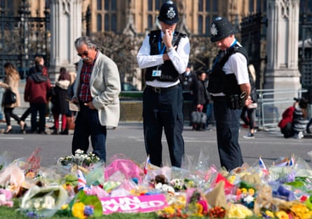 Police officers stop to look at floral tributes to the victims near the Houses of Parliament in Westminster.