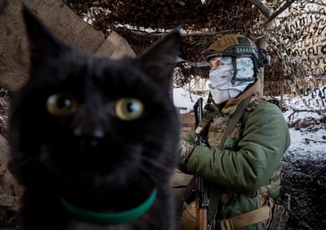 A Ukrainian serviceman stands at his position in a trench, as a cat looks on, at a frontline in the Sumy region near the border with Russia.