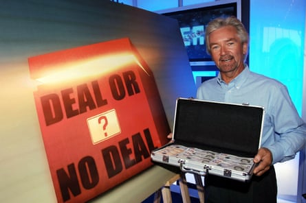 Noel Edmonds with a suitcase full of money in front of a Deal or No Deal? sign.