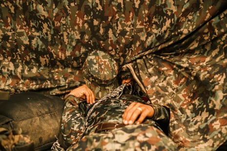 A fighter in camouflage gear asleep with their cap over their face in a tent of the same material