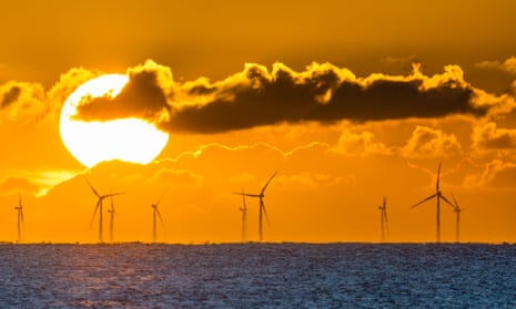 The sun rises over offshore windfarm turbines in the sea off the south coast of England.