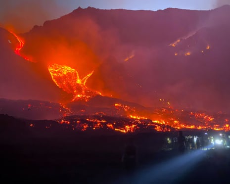 People gather to watch as lava flows down Mount Etna during a period of heightened volcanic activity, near Catania, Sicily.