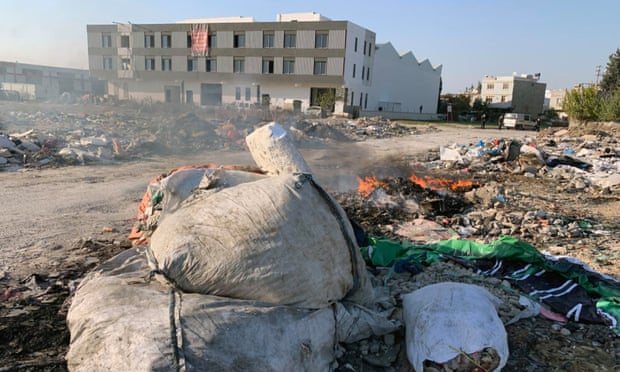 a patch of wasteland with bags of rubbish and fires smouldering