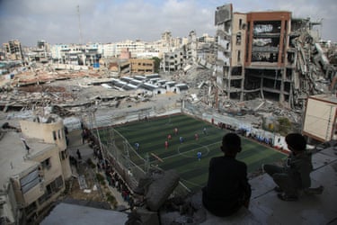 Children sit high in a bombed building watching the football match down below