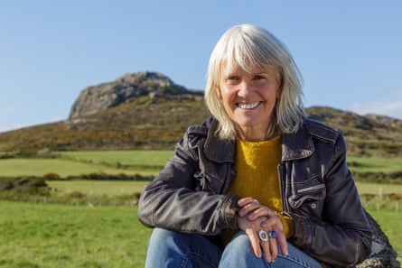 Nicola Davies sitting outdoors and smiling, with green fields and a hillside behind her