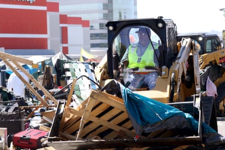 A person in a bulldozer scoops up wooden pallets and tarps.