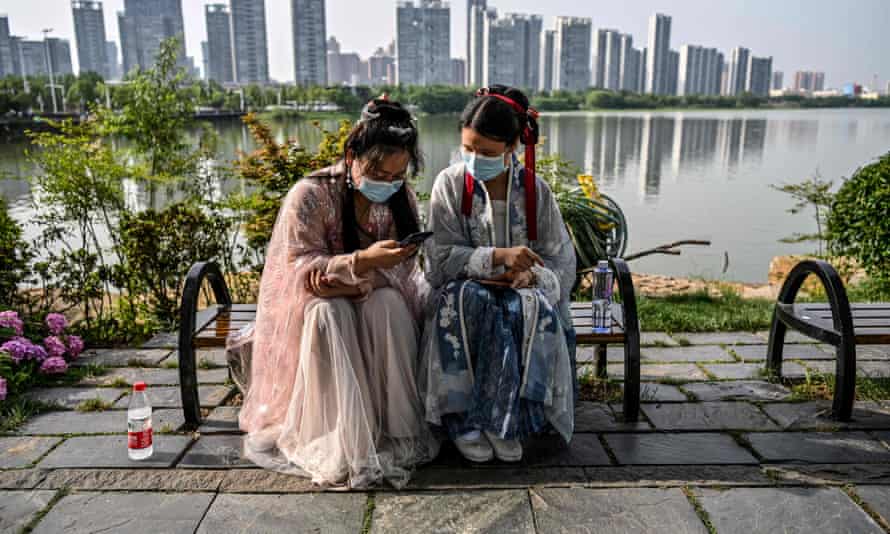 Women in facemasks and traditional costumes of Song dynasty and Tang dynasty are seated on a bench in a park next to the East Lake, Wuhan.