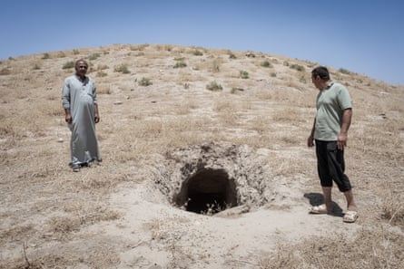 Two men stand next to a large hole in a barren landscape