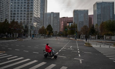 A woman drives a scooter across a nearly empty intersection in the central business district of Beijing, China. 