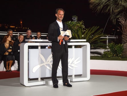 A man in a black suit stands with an award on stage.