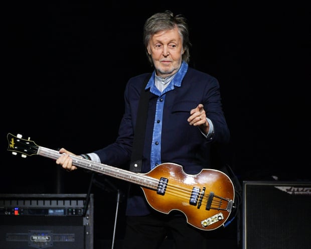 Paul McCartney pointing and player a guitar on stage