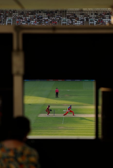 England's Heather Knight reverse sweeps as a scorer watches through a window in the scoreboard.