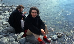 George Harrison and John Lennon sit on rocks by a river in Rishikesh while studying transcendental meditation.