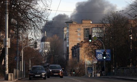 Cars drive down the street while smoke rises from a fire after a rocket attack in the centre of Kyiv on December 29, 2023.