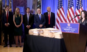 Donald Trump, accompanied by Mike Pence and family members stands behind piles of documents purportedly detailing his actions to divest himself of his business interests.