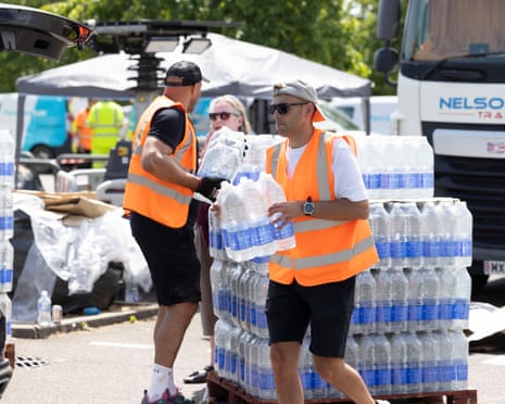Workers in high-visibility vests carry packs of bottled water at a Whitstable distribution point
