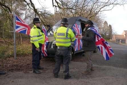 Two police officers speaks to a man with a union jack draped over his shoulders