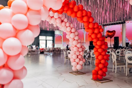 A pink and red balloon arch decoration in a party hall, with heart-shaped balloons