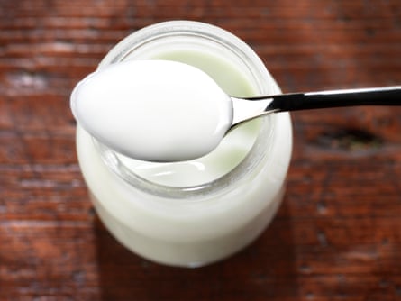 Spoonful of yoghurt over a glass jar on a wooden surface