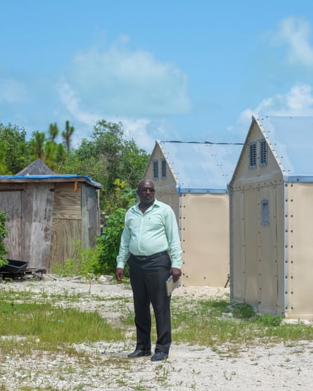 a man in a mint green shirt stands outside small structures with blue roofs