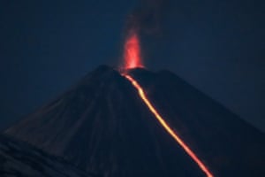 A night shot of a molten lava spewing from a volcano's crater and running down its side
