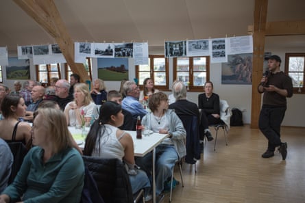 People sitting at tables listen to a man standing speaking into a microphone