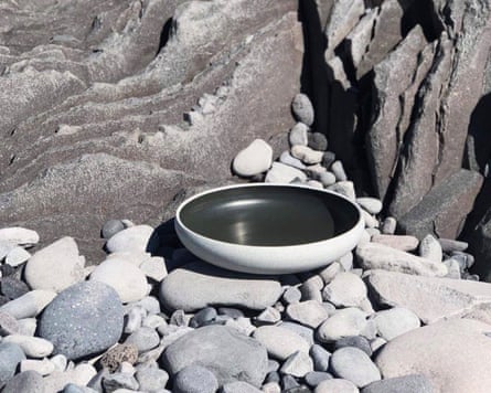 A porcelain bowl using volcanic ash resting on pebbles against a backdrop of grey rock
