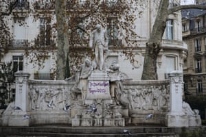 Pigeons fly past a statue with a graffiti reading ‘popular insurrection’, near the Arc de Triomphe