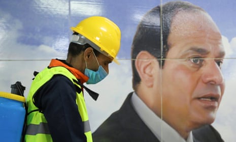 A man sprays disinfectant on a street in Cairo, by a banner of Egyptian president Abdel Fatah al-Sisi.