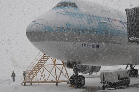 Workers stand next to a Korean Air plane parked on the tarmac during snowfall at Incheon international airport