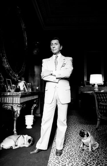 Valentino stands with his two pugs on the floor by his feet