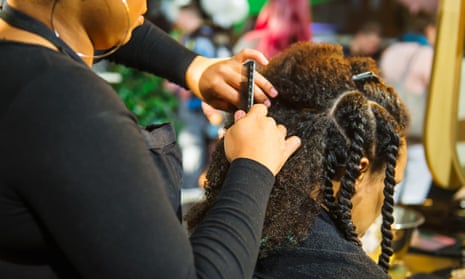 Hair stylist works on braided hair of a black woman.