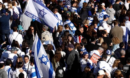 Overhead crowd shot of people wearing mostly white and blue winter clothes and waving Israeli flags.