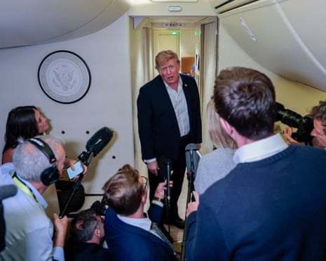 Man in suit leans through doorway into gaggle of reporters holding microphones.