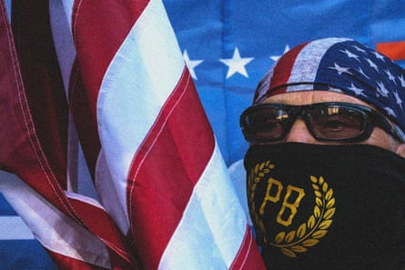 man next to american flag wearing bandanna over mouth that says ‘PB’