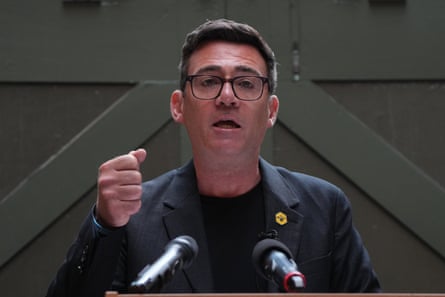 Andy Burnham makes a speech in a black jacket against a green wooden door