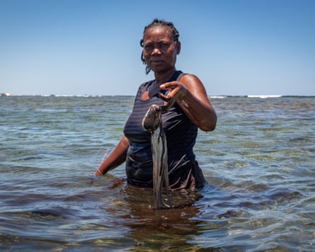 An African woman stands in waist-deep sea holding up an octopus
