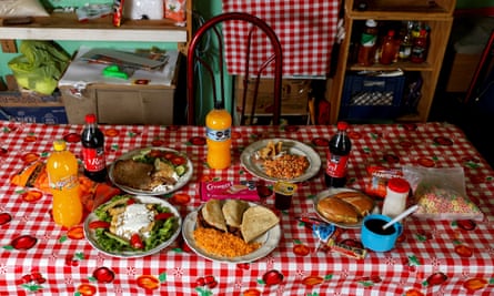 A table with five plates of food, four bottles of sweet fizzy drinks, biscuits and other ultra-processed food