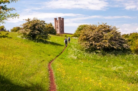 two distant fgurs hiking towards an old tower, in a green suumer English field