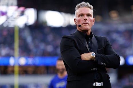Pat McAfee stands with arms crossed, wearing a headset microphone, on the field before a game