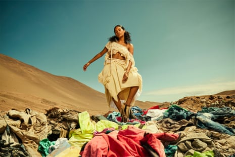 Model dressed in white clothes salvaged from the Atacama dump stands on a pile of clothes in the desert