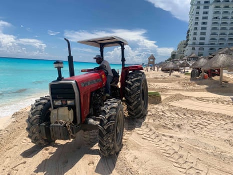 A tractor moves sand on a beach near a high-rise building