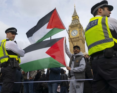 Protesters hold Palestinian flags while two police officers with backs to camera look on with Big Ben clock visible behind.