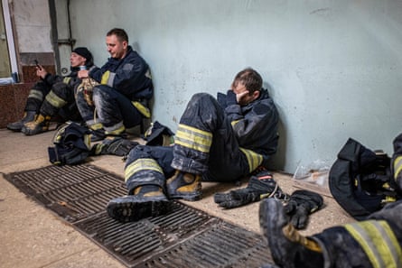 Firefighters take a break sitting against a wall