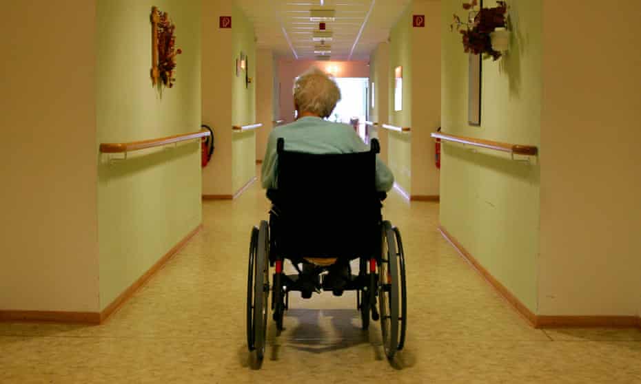 Old man in a wheelchair in the corridor of a retirement home, facing away from the camera