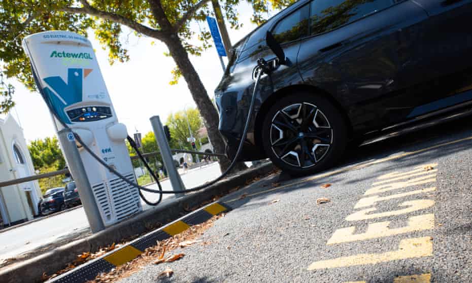 A black electric car is plugged into a charging station