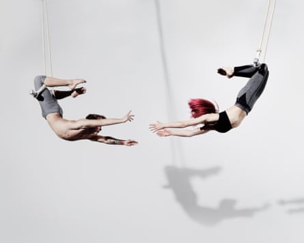 Circus artists on a trapeze, with their shadows projected on a white wall.