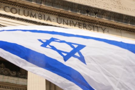 The white Israeli flag, with a blue star of David between two blue lines, in front of a building inscribed with the words Columbia University.