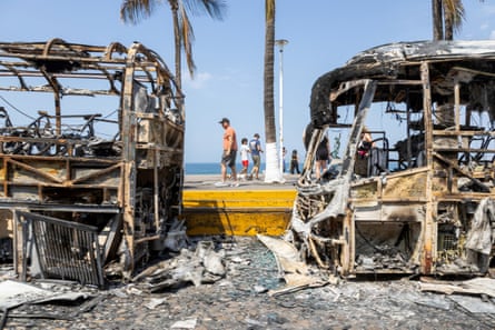people walk past burned buses