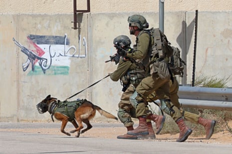 Two heavily armed soldiers run behind a muzzled dog.
